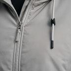 Closeup of light grey windbreaker jacket fabric, zip and hood drawstring detail
