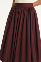 Close-up of burgundy pleated midi skirt waistband and pleat detail